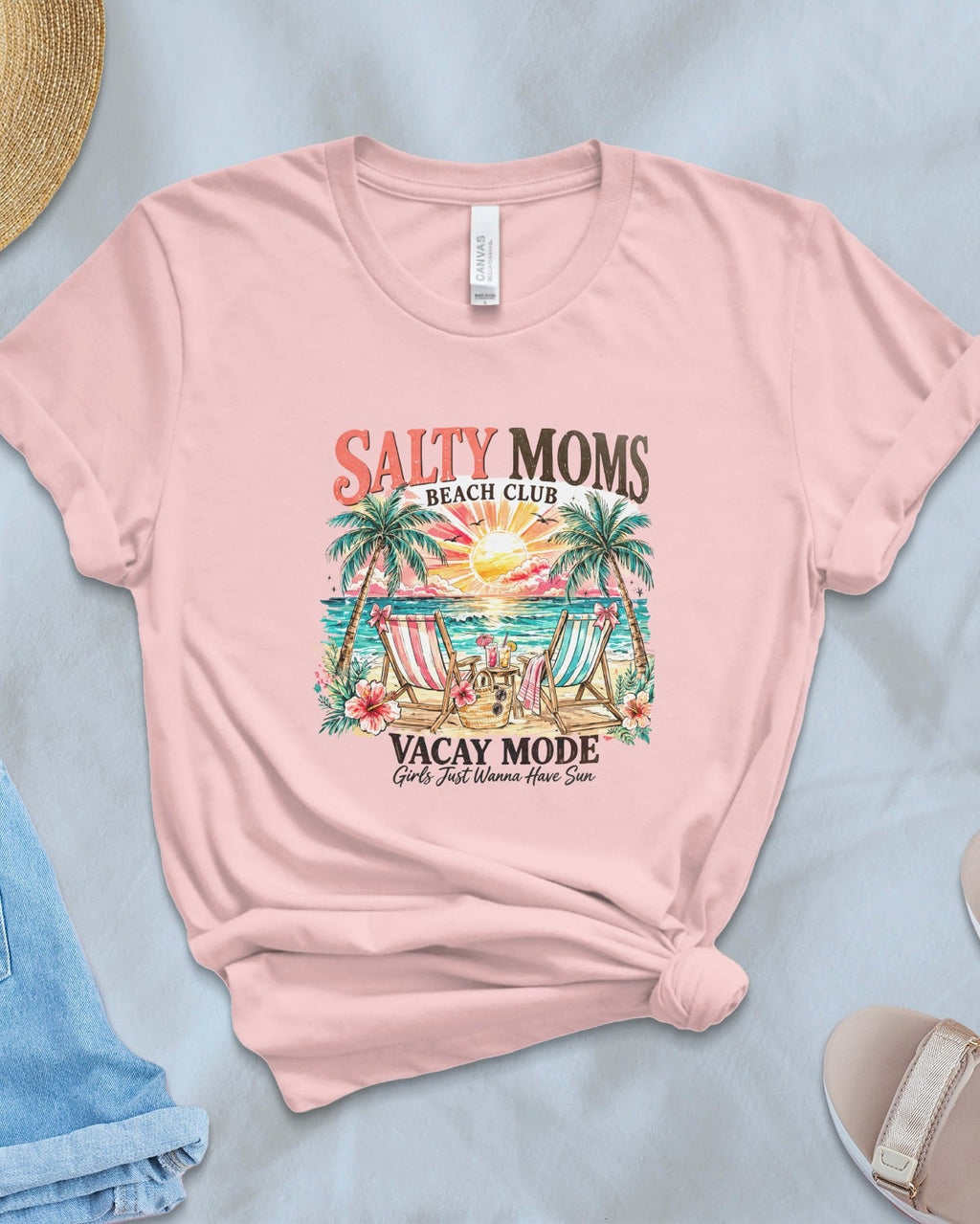 Pink t-shirt with 'Salty Moms' graphic design on a light blue surface with accessories.