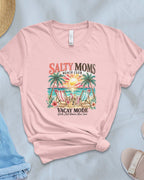 Pink t-shirt with 'Salty Moms' graphic design on a light blue surface with accessories.