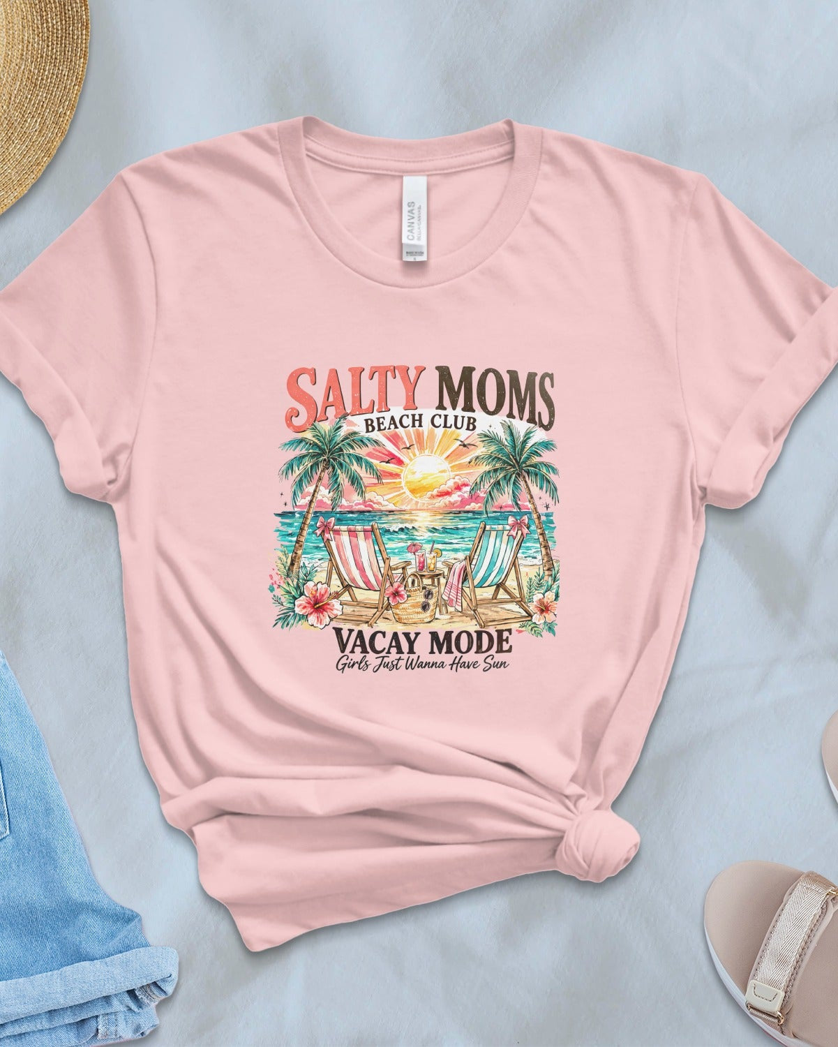Pink t-shirt with 'Salty Moms' graphic design on a light blue surface with accessories.