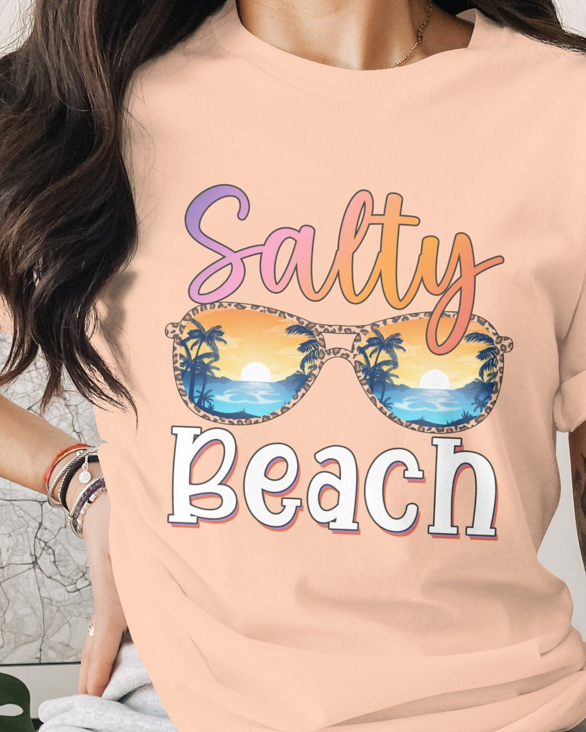 Person wearing a peach t-shirt with 'Salty Beach' and sunglasses graphic.