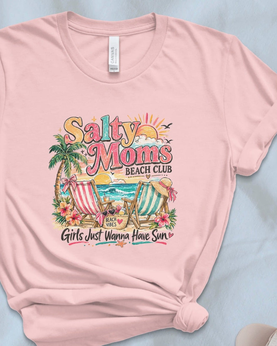 Pink t-shirt with 'Salty Moms Beach Club' design on a light blue surface with accessories.
