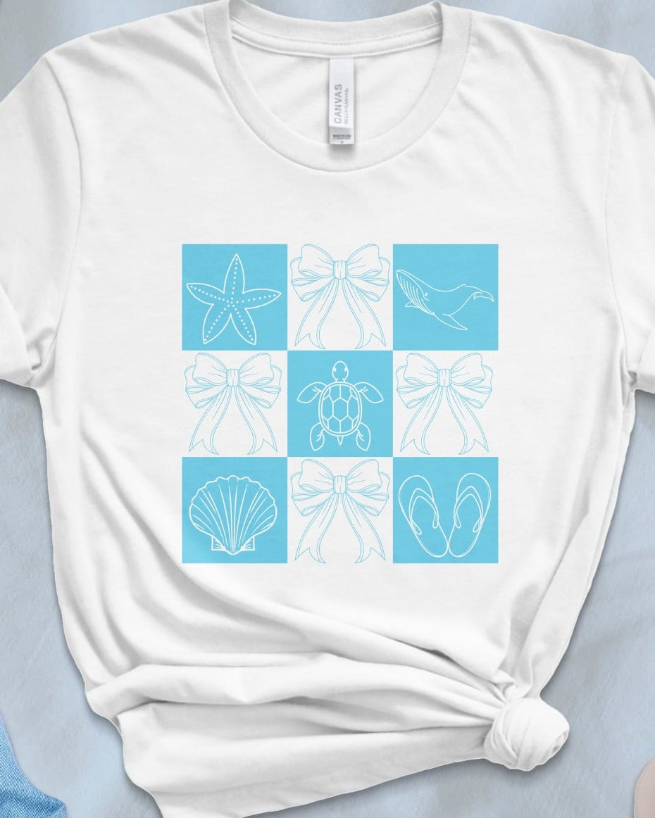 White t-shirt with blue sea-themed graphic on a light blue surface with accessories.