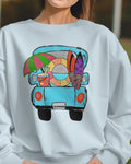 Person wearing a light blue sweatshirt with a colorful graphic of a van on a grassy background