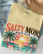 Beige t-shirt with 'Salty Moms Beach Club' design on a denim jacket and straw hat.