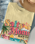 Beige t-shirt with 'Salty Moms Beach Club' design, denim jacket, and beige hat on a light gray background