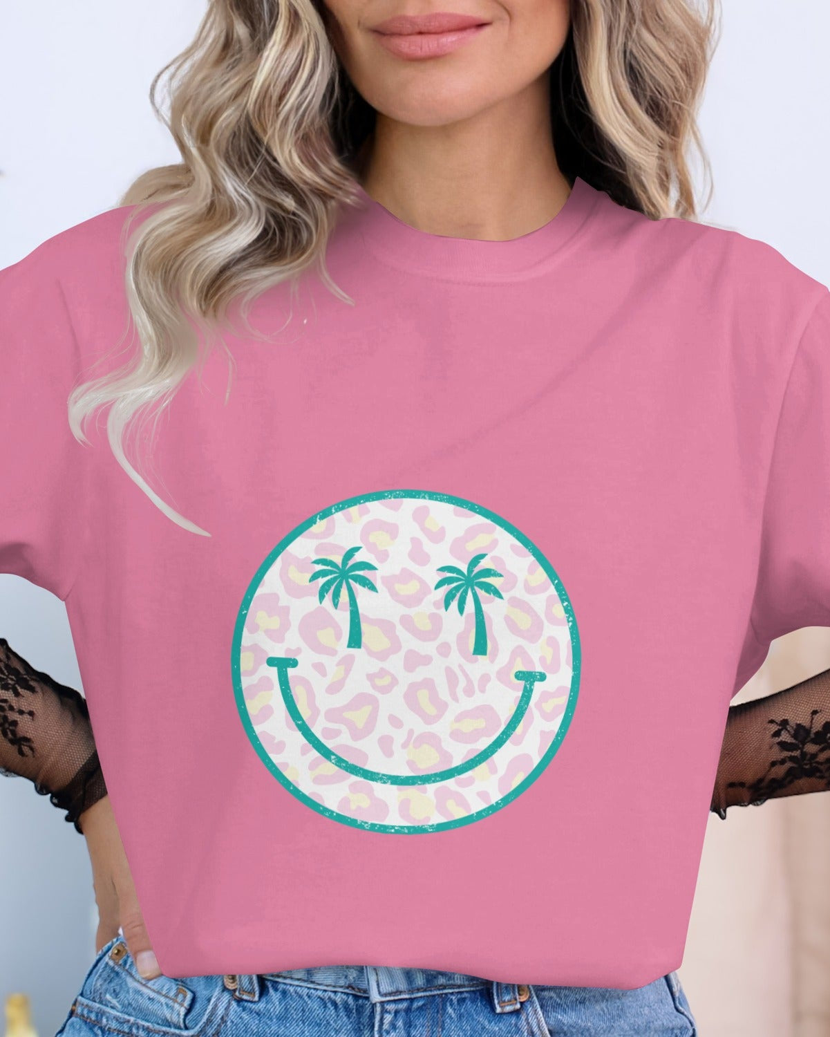 Person wearing a pink t-shirt with a smiley face design featuring palm trees.