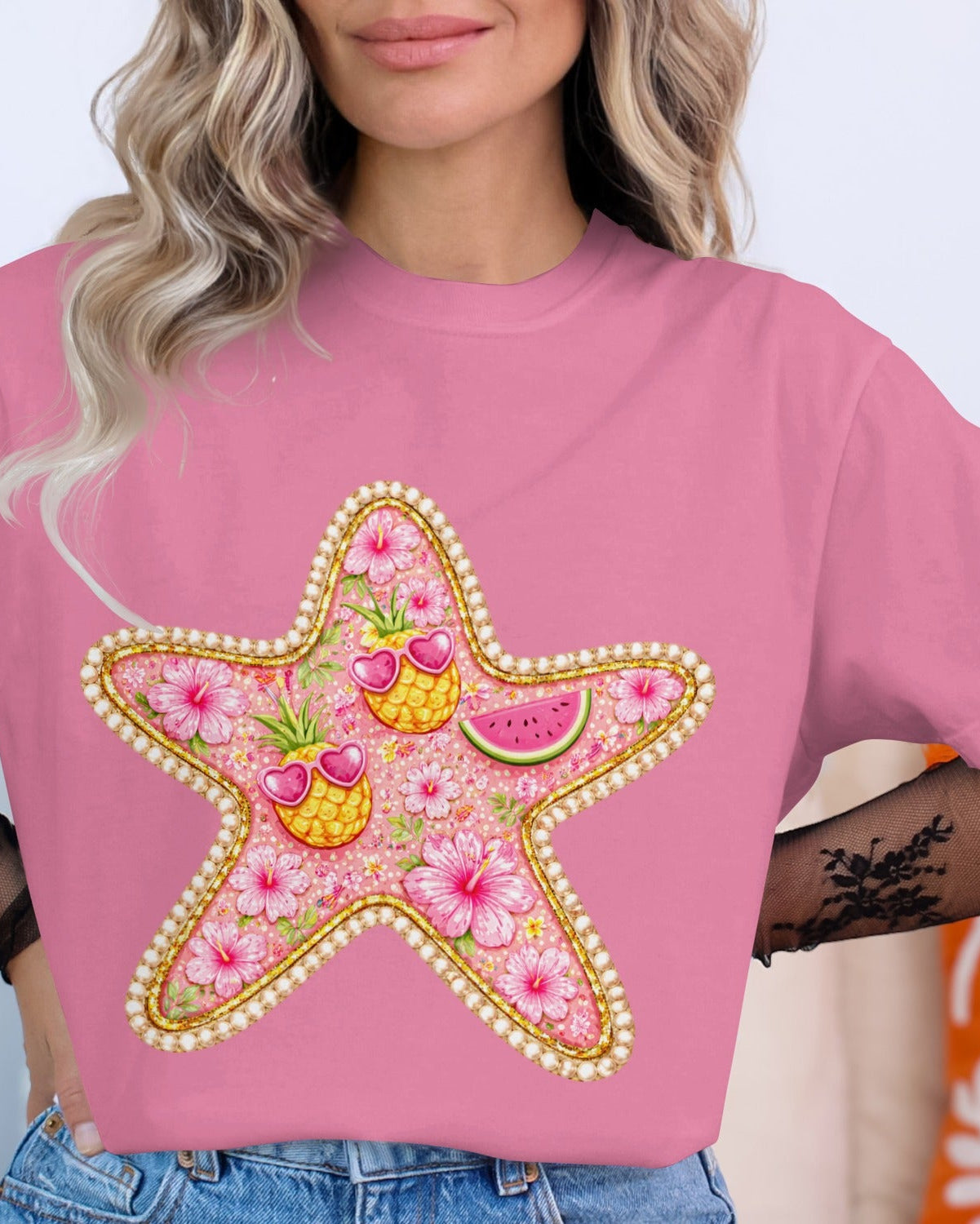 Person wearing a pink t-shirt with a decorative starfish design featuring flowers and fruits.