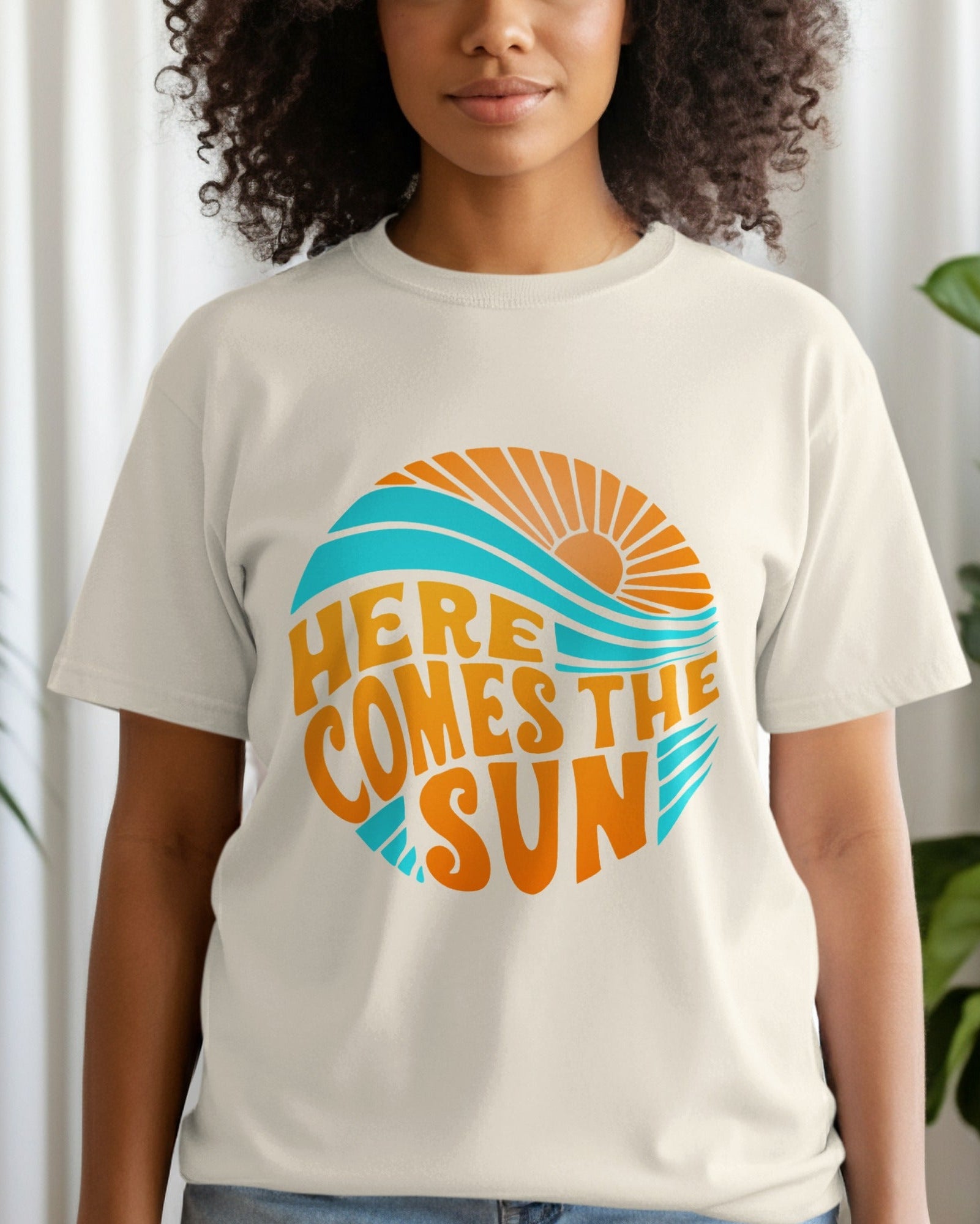 Person wearing a t-shirt with 'Here Comes the Sun' design in a room with plants.