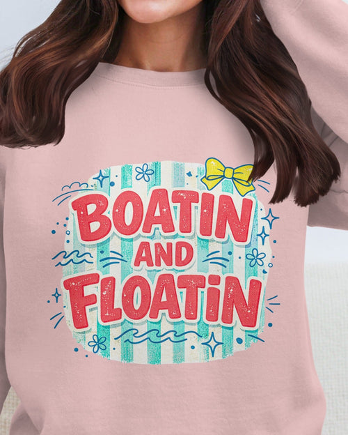 Pink sweatshirt with 'Boatin and Floatin' text and graphics on a plain background