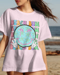 Person wearing a 'Beach Bum' t-shirt with a smiley face design on a beach.