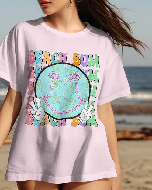 Person wearing a 'Beach Bum' t-shirt with a smiley face design on a beach.