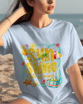 Woman wearing a white t-shirt with 'Sunshine of my Life' design on a beach.
