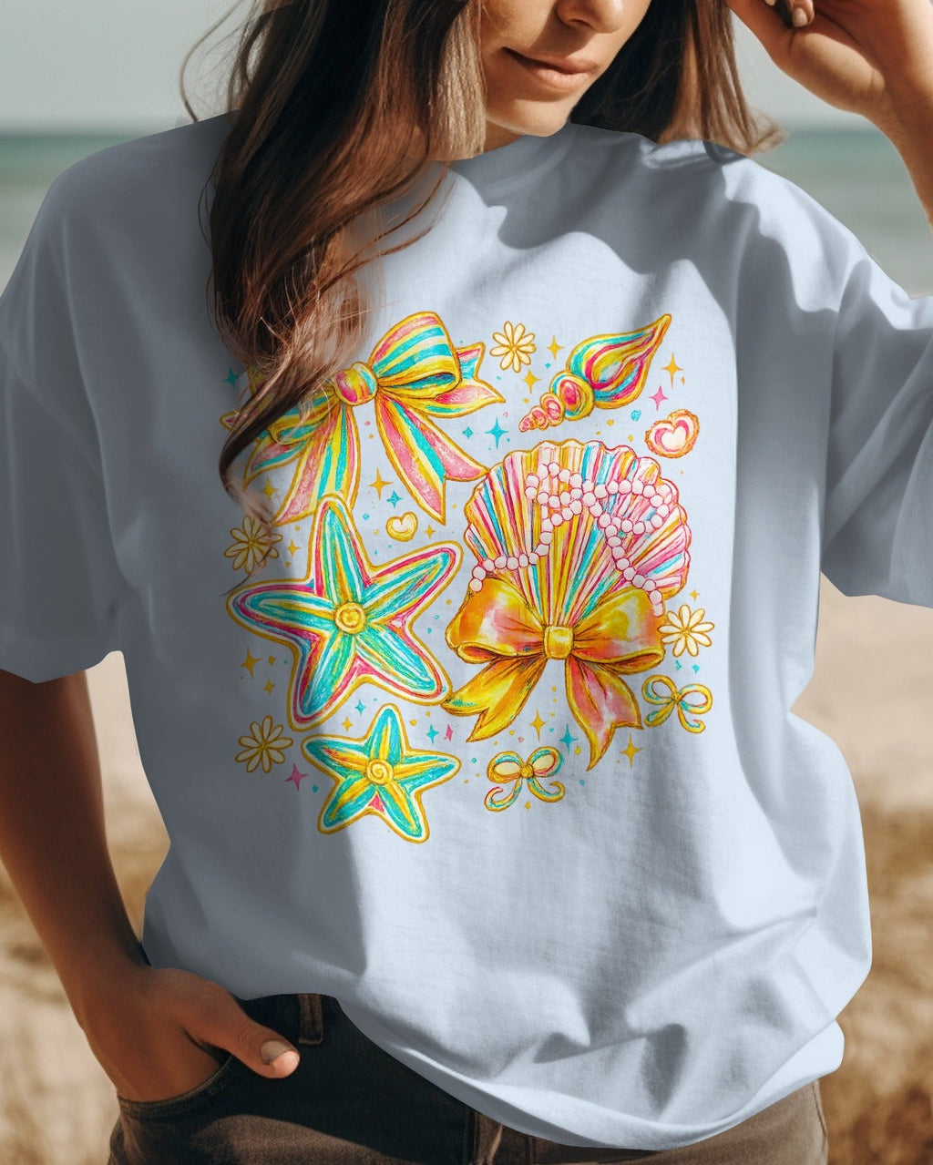 Person wearing a light blue t-shirt with colorful starfish design on a beach.