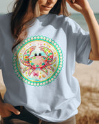 Person wearing a white t-shirt with a colorful crab design on a beach.