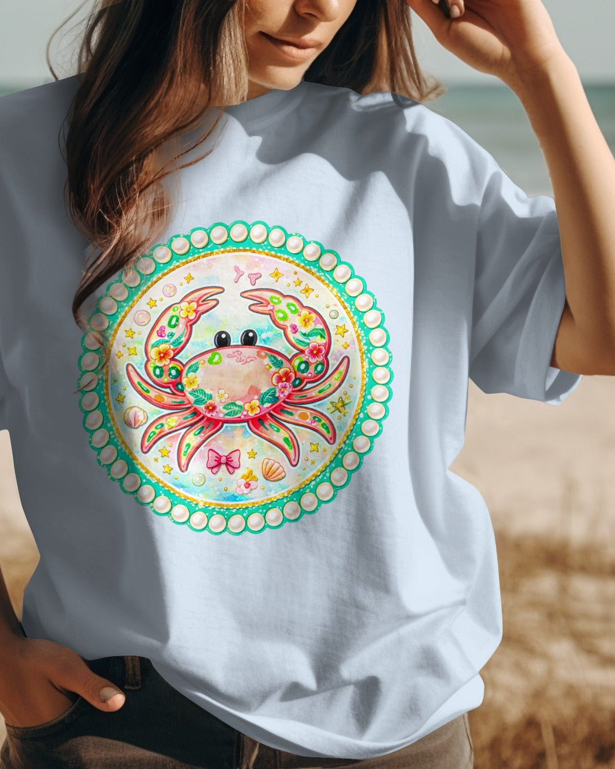 Person wearing a white t-shirt with a colorful crab design on a beach.