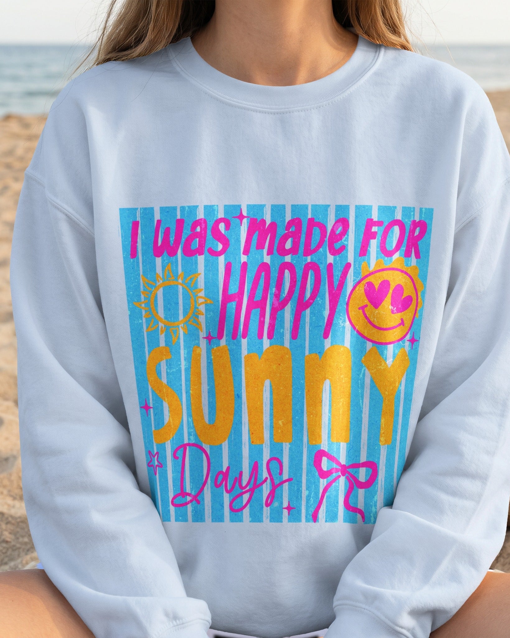 Person wearing a light blue sweatshirt with colorful text and graphics on a beach.