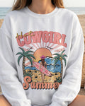 White sweatshirt with 'Hot Cowgirl Summer' graphic design on a beach.