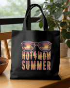 Black tote bag with 'HOTEL MOM SUMMER' design on a wooden table.