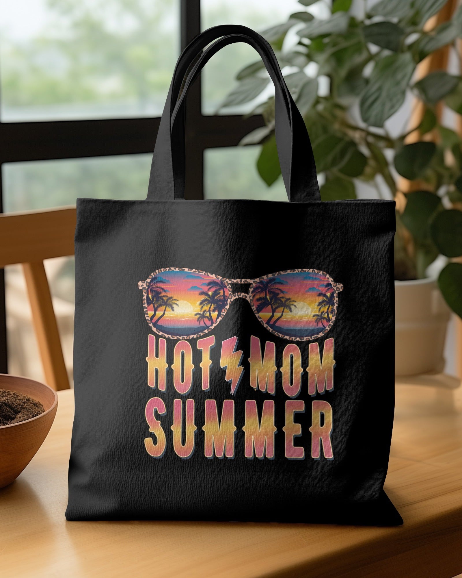 Black tote bag with 'HOTEL MOM SUMMER' design on a wooden table.