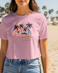 Person wearing a pink 'Summer Vibes' t-shirt with palm trees and a rainbow on a beach.