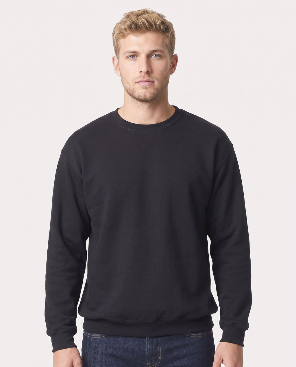 A man wearing a plain black crewneck sweatshirt and dark blue jeans, standing against a light gray studio background.