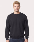 A man wearing a plain black crewneck sweatshirt and dark blue jeans, standing against a light gray studio background.