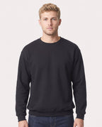 A man wearing a plain black crewneck sweatshirt and dark blue jeans, standing against a light gray studio background.