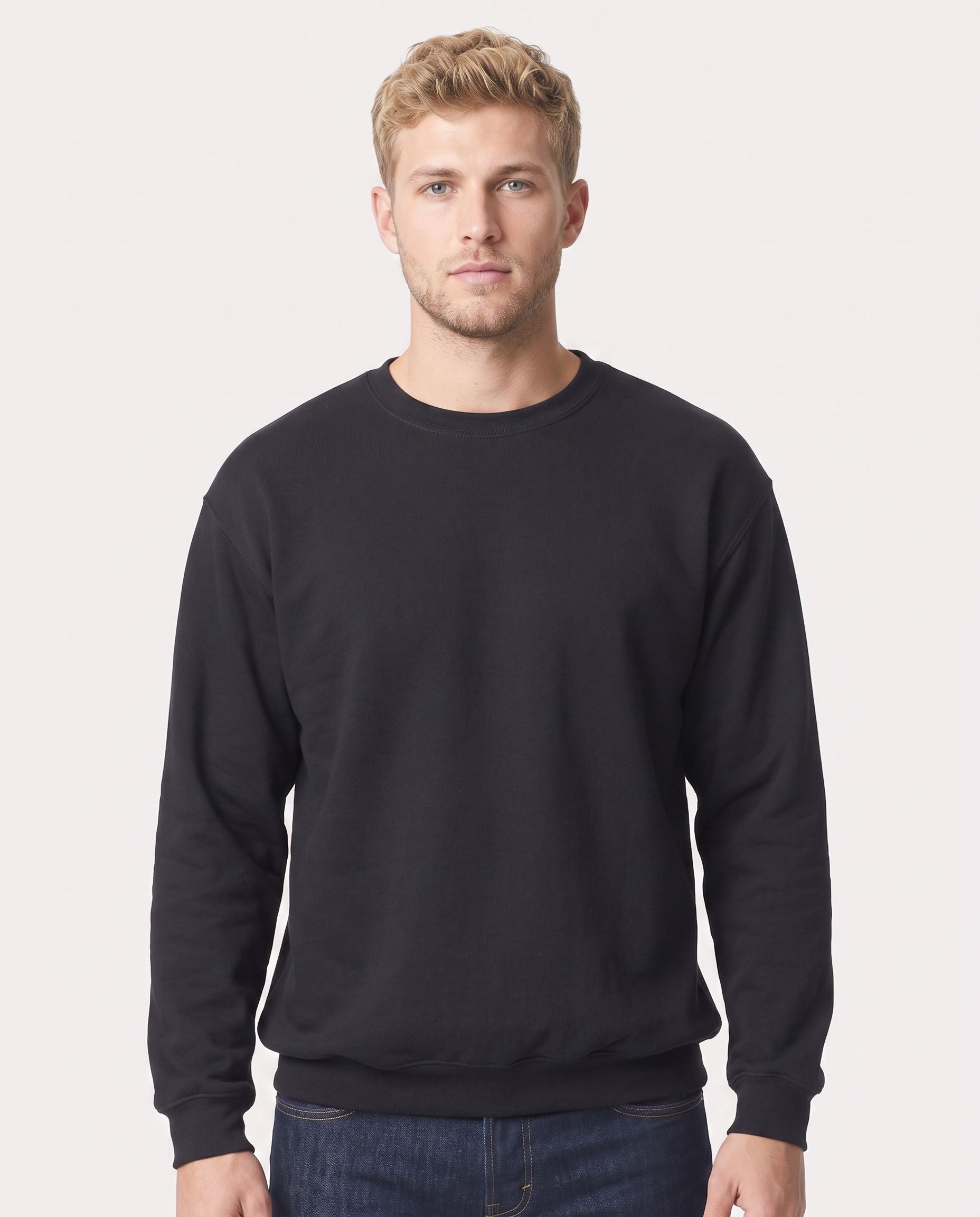 A man wearing a plain black crewneck sweatshirt and dark blue jeans, standing against a light gray studio background.